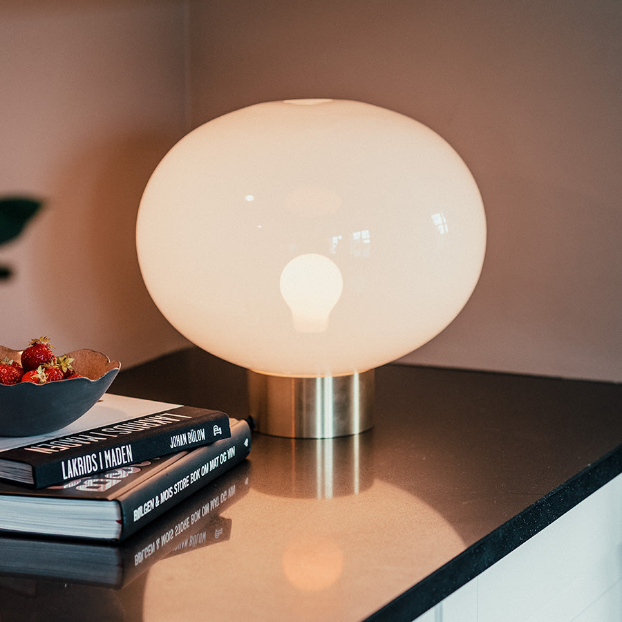 Elegant bordlampe med stor hvit glasskuppel og messing sokkel, ser stilig ut på en bordflate med bøker.