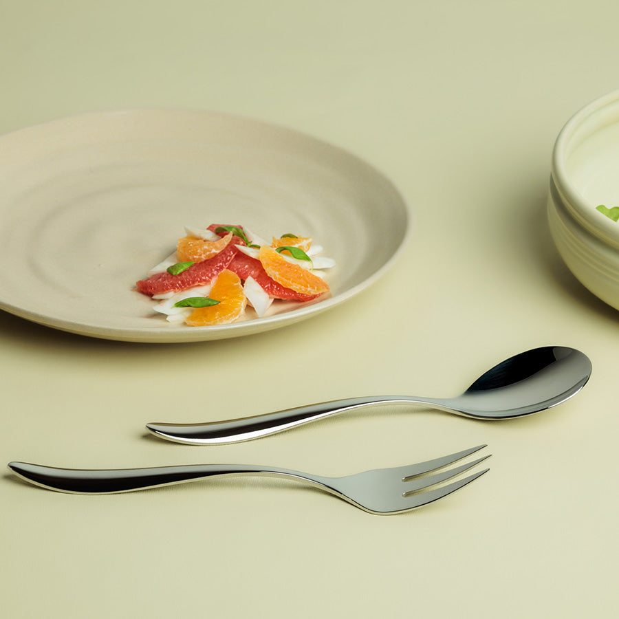 Serveringsbestikk Lykke, med en elegant serveringsgaffel og serveringsskje plassert ved siden av en delikat rett på tallerken.