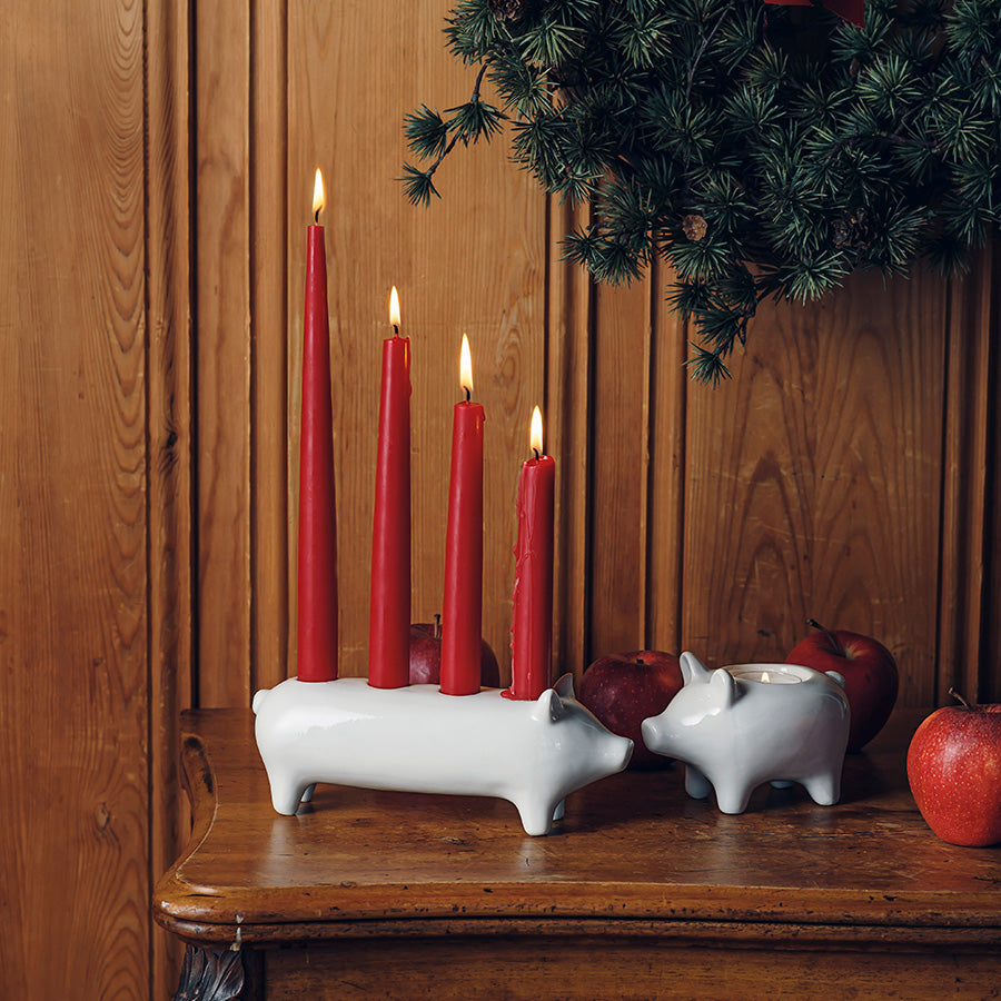 Heldiggrisen Adventsstake fra Porsgrunds Porselænsfabrik i en juledekorasjon med røde lys på et trebord.