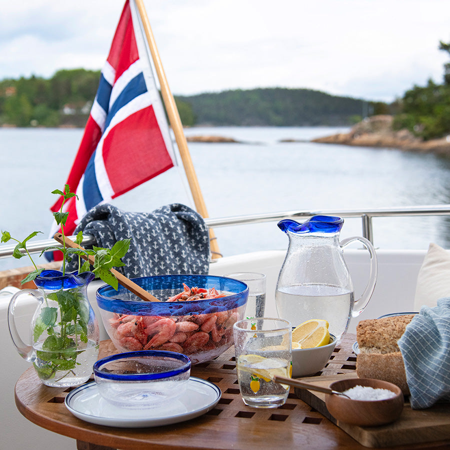 Hadeland Glassverk Skjærgård bolle i bruk på en vakker brygge med reker, lemoan og vann, med norsk flagg i bakgrunnen.