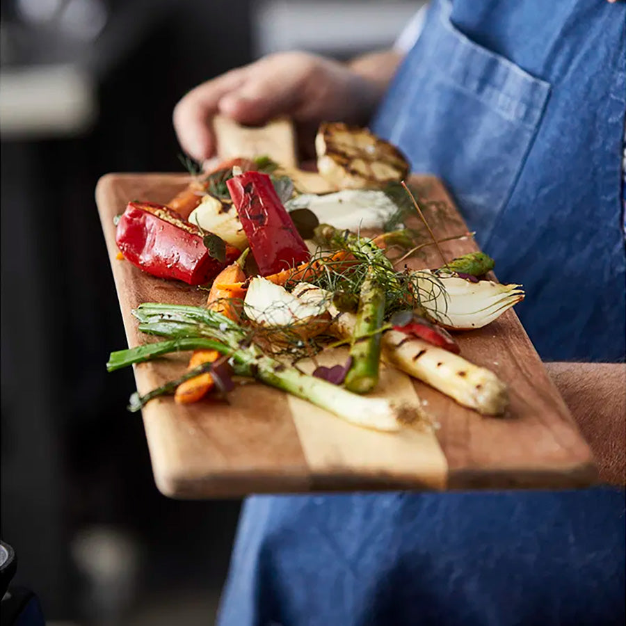 Person som holder et serveringsbrett med grillet grønnsaker, ideelt for festlige sammenkomster.