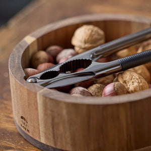 Nærbilde av en nøtteknekker i metall plassert i en skål fylt med nøtter, dekorativt og funksjonelt.
