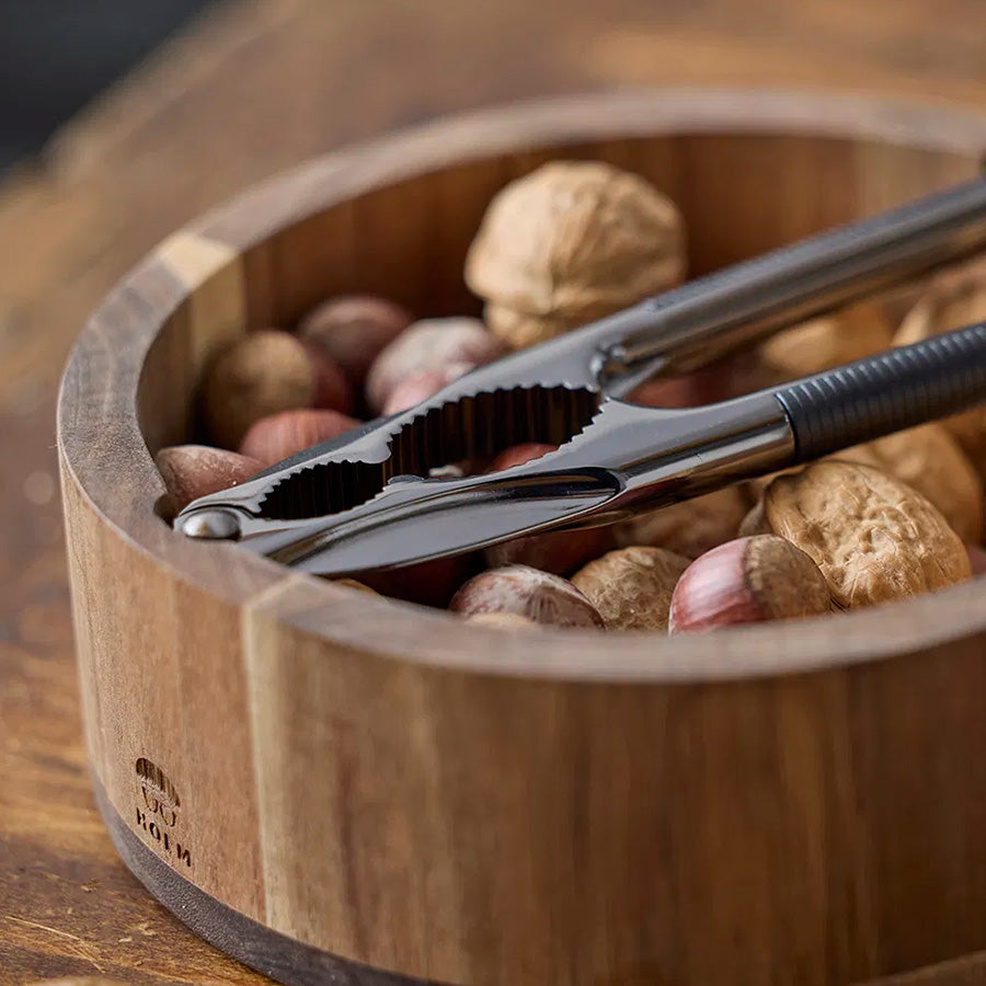 Nærbilde av en nøtteknekker i metall plassert i en skål fylt med nøtter, dekorativt og funksjonelt.