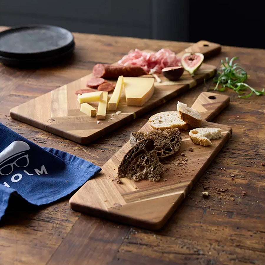Holm Serveringsbrett Fiksebensmønster 55x20cm Akasie, trefjøl med ulike brød og deli-produkter på et elegante bord.