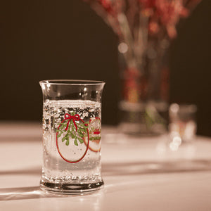 Julevannglass fra Holmegaard med sprudlende drikke, dekorert med festlige julebånd og misteltein.