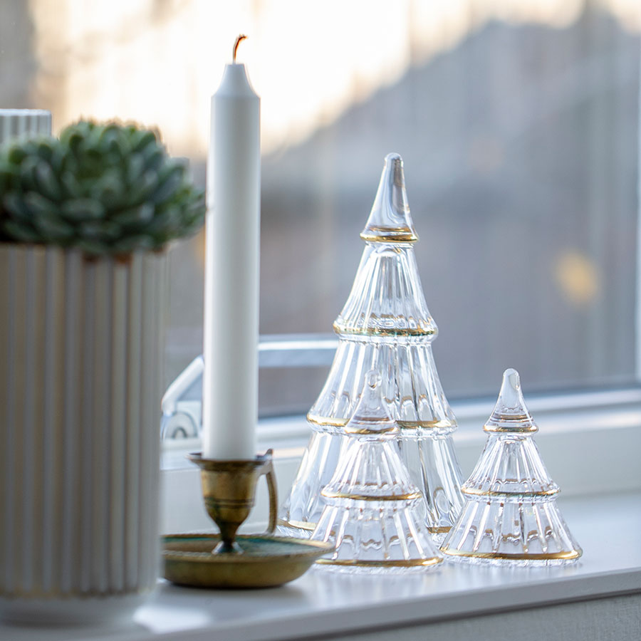 Holmegaard Fairytales juletre i glass, to størrelser plassert på et vindu med lys og grønn dekor, perfekt juledekorasjonsidé.