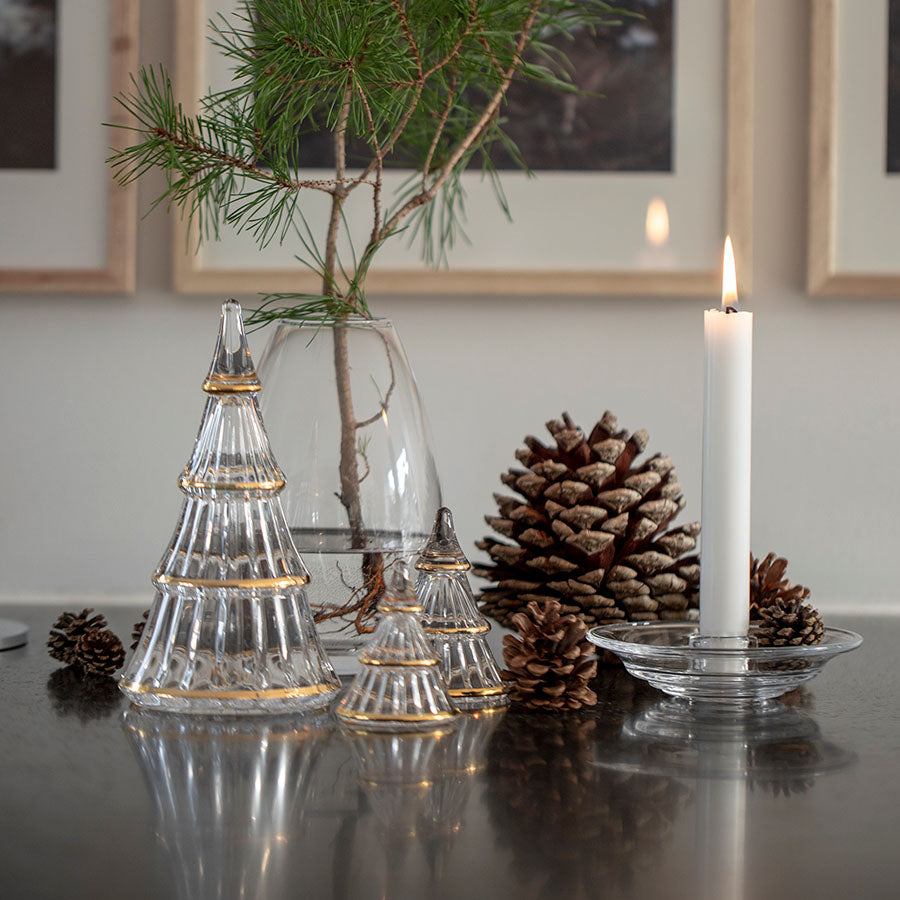Holmegaard Fairytales juletre i klart glass, satt på et bord med kongler, lys og grønt, som en stilfull del av julepynt.