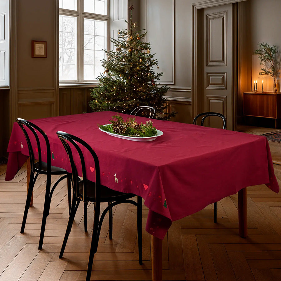 Julerød juleduk fra JUNA dekket på spisebord i julepyntet hjem med juletre og broderte julemotiver