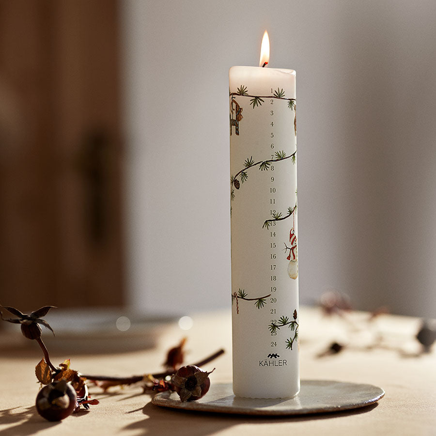 Hammershøi Jul kalenderlys brennende i et moderne hjem, prydet med juleillustrasjoner og grønt, perfekt for nedtelling til julaften.