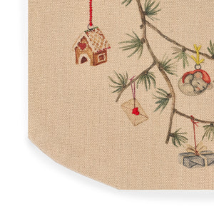 Nærbilde av sandfarget julesokk med detaljerte broderier av julehus, gaver og grangren