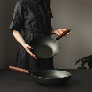 To Antei Kazan wokpanner holdt av en person, den ene i hendene og den andre på bordet.