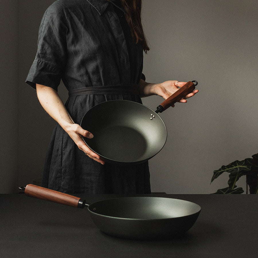 To Antei Kazan wokpanner holdt av en person, den ene i hendene og den andre på bordet.