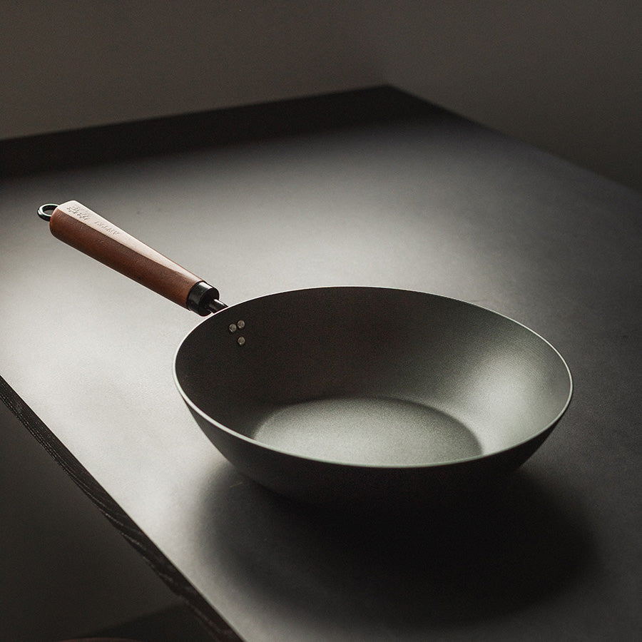 Nærbilde av Antei Kazan wokpanner i karbonstål med et stilrent design og ergonomisk valnøtthåndtak.