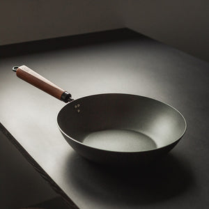 Nærbilde av Antei Kazan wokpanner i karbonstål med et stilrent design og ergonomisk valnøtthåndtak.
