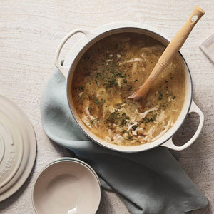 Le Creuset støpejernsgryte med kylling- og urtesuppe, servert med en tre-skje, illustrerer gryten i bruk.