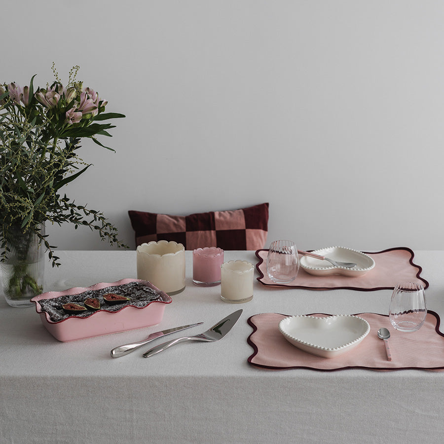 Bordoppsett med flere rosa telysholdere, inkludert dekorative elementer som servise og blomster, som skaper en koselig atmosfære.