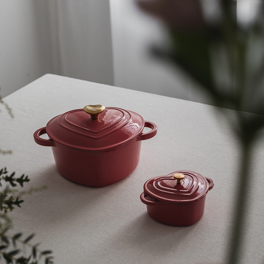 To støpejernsformer i hjerteform, en stor og en liten, i bringebær-rød farge, utstilt på ett elegant bord.