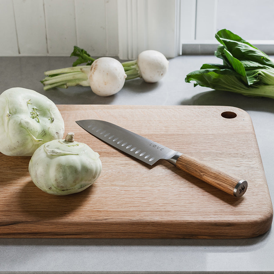 Løve Steig Santoku kniv i bruk på et skjærebrett med friske grønnsaker, den perfekte kniven for matlaging med effektivt og stilrent design.