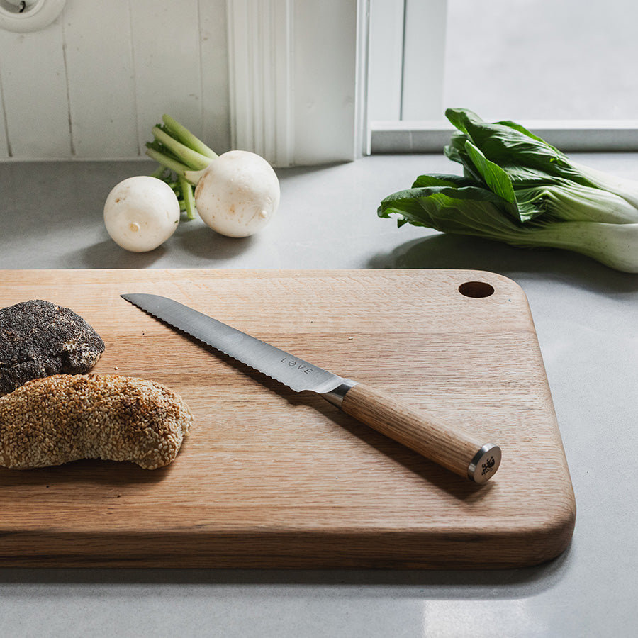 Løve Steig Brødkniv 19 cm på et skjærefjøl med ferskt brød og grønnsaker, som viser knivens allsidighet og stil.