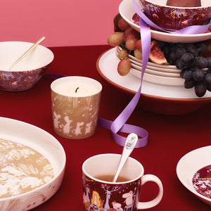 Moomin Arabia Festlige Stunder Mummi stearinlys plassert på et dekkt bord med Mummi-servise og frukt, som skaper en koselig atmosfære for festlige anledninger.