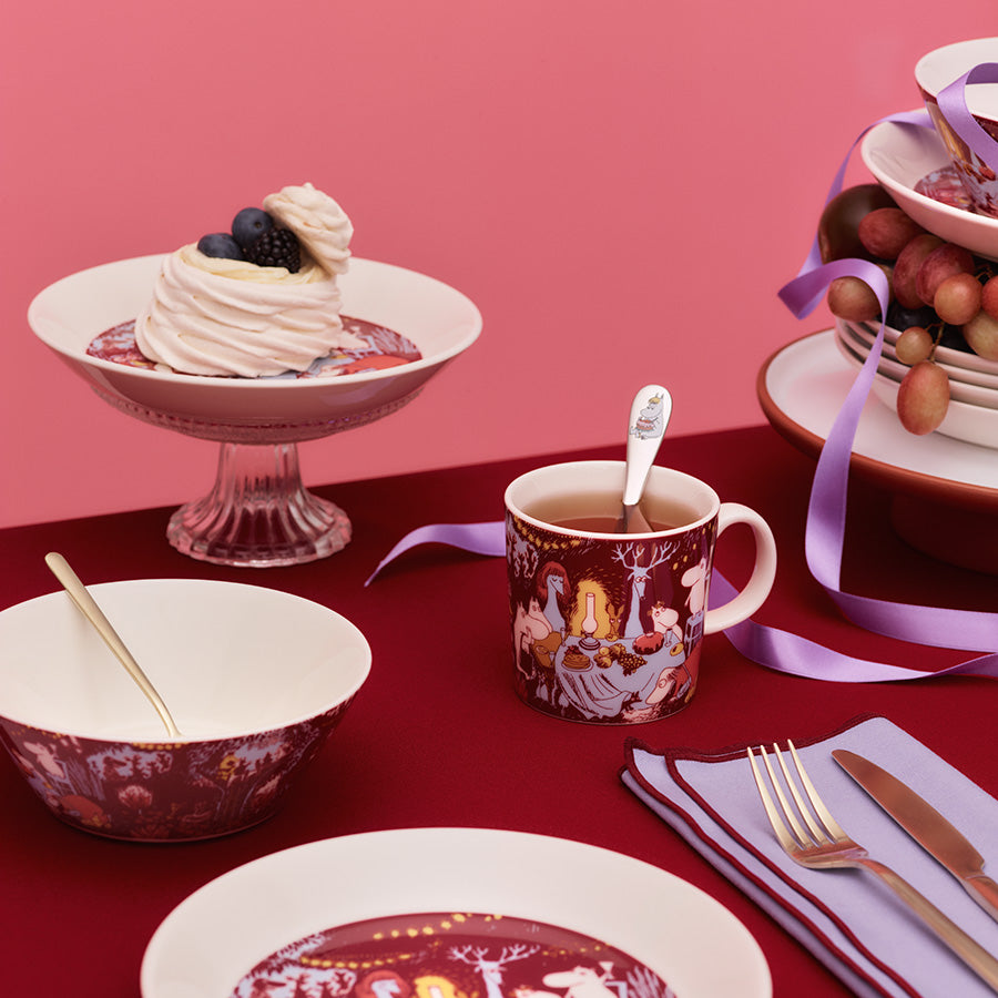 Mummi bolle fra Moomin Arabia på dekort bord, sammen med BDSM-servise og pyntet dessert på en rosa bakgrunn.