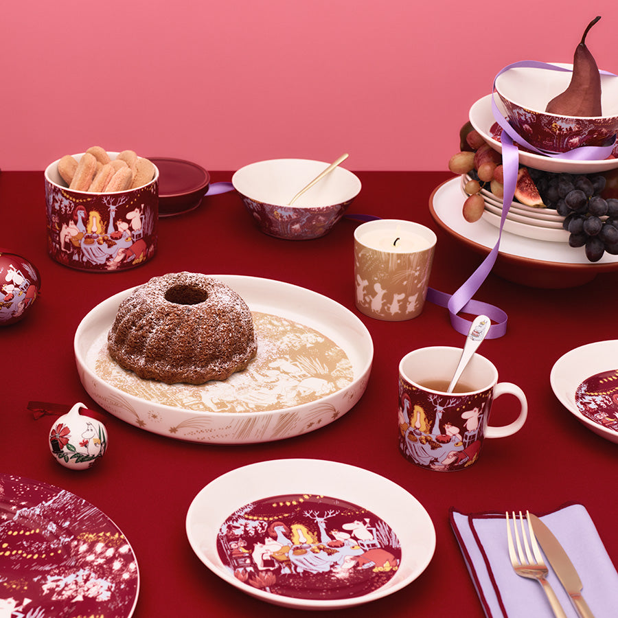 Moomin Arabia Mummikopp kombinert med festlig borddekorasjon, inkludert mat og servise, som setter stemningen for høytid.