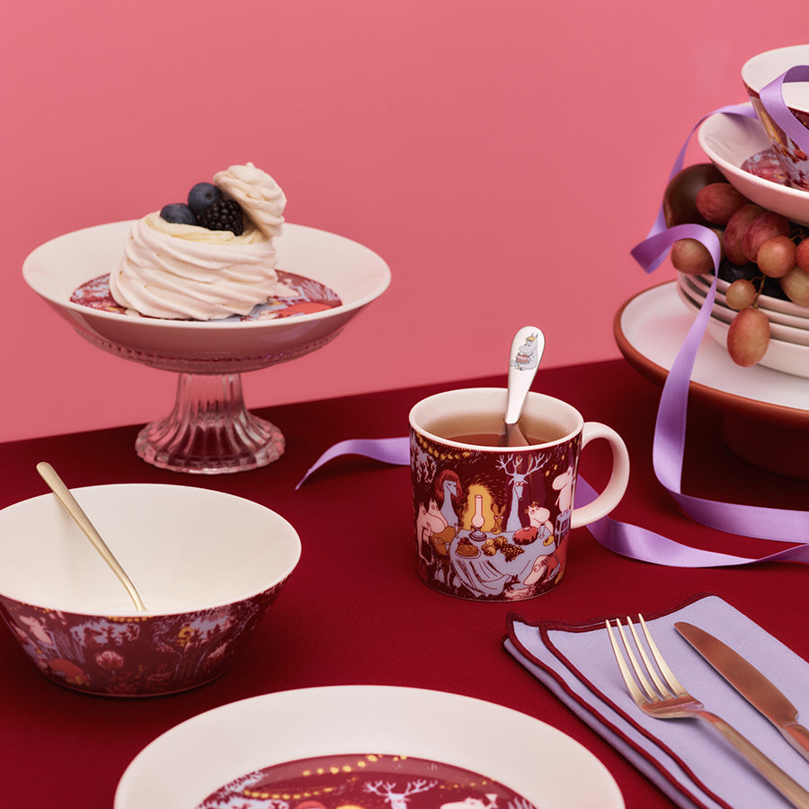 Moomin Arabia Mummikopp plassert på et bord dekket med festlig dekor, med en dessert og tallerkener, perfekt for feiring.