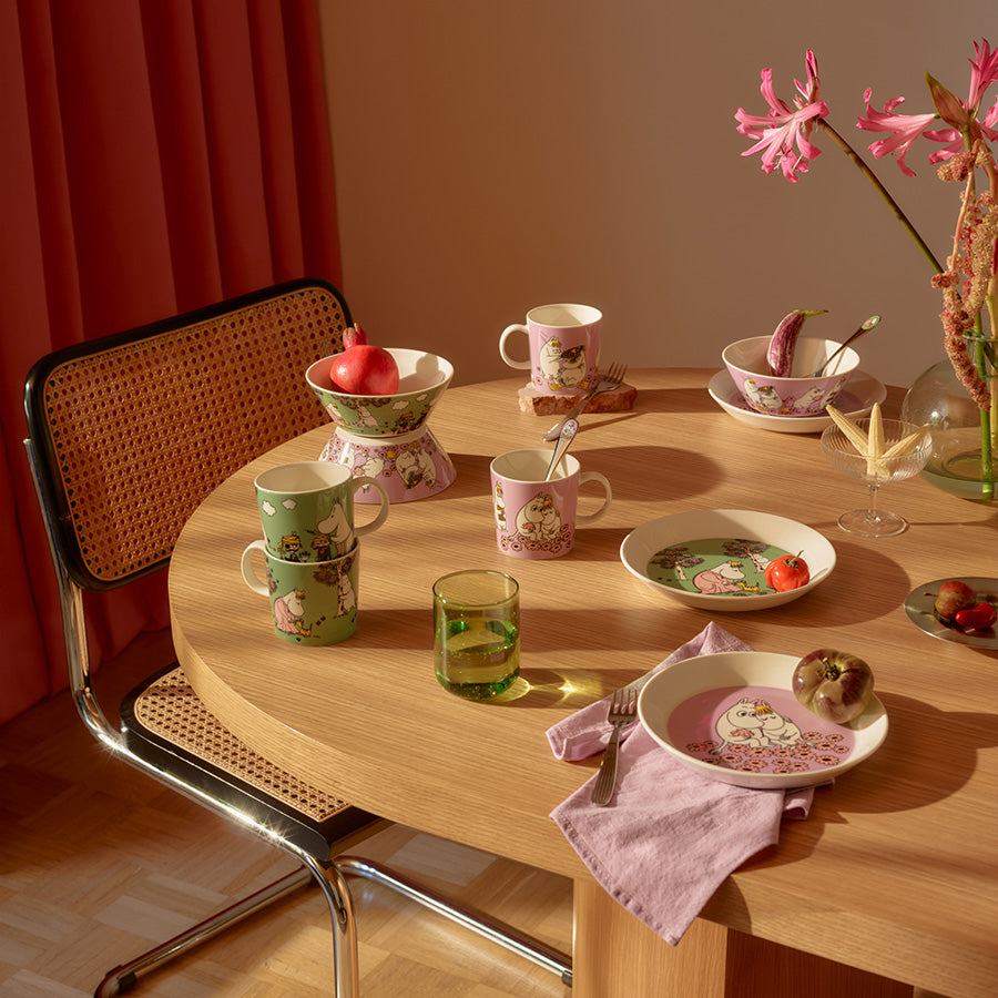 Stilfull borddekking med Mummi asjett, kopper og skåler i grønne og rosa farger, ideell for en koselig samling rundt bordet.