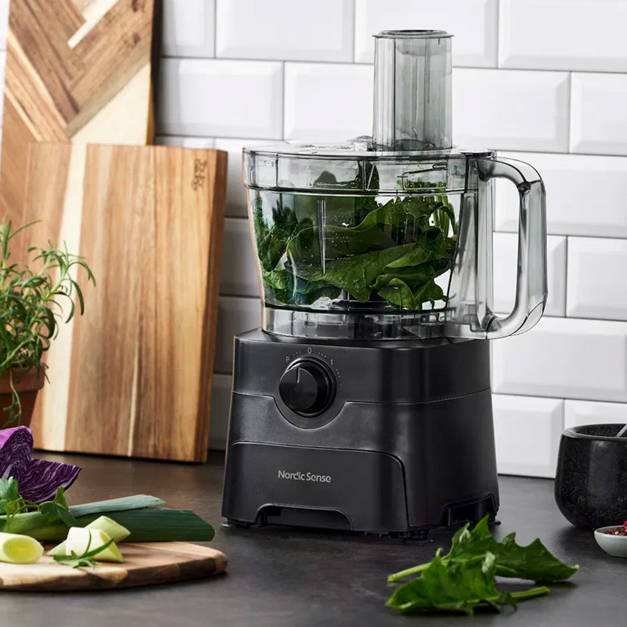 Nordic Sense foodprossessor i bruk med grønne ingredienser i bollen, illustrerer allsidigheten i matforberedelse.