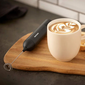 Svart Nordic Sense melkeskummer ved siden av en kopp cappuccino med melkeskum