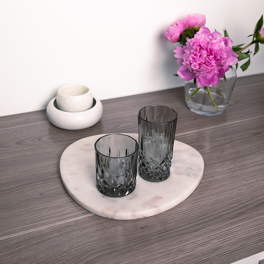 To elegante grå longdrinkglass plassert på en marmorplate, dekorert med blomster, som fremhever deres stil og design.