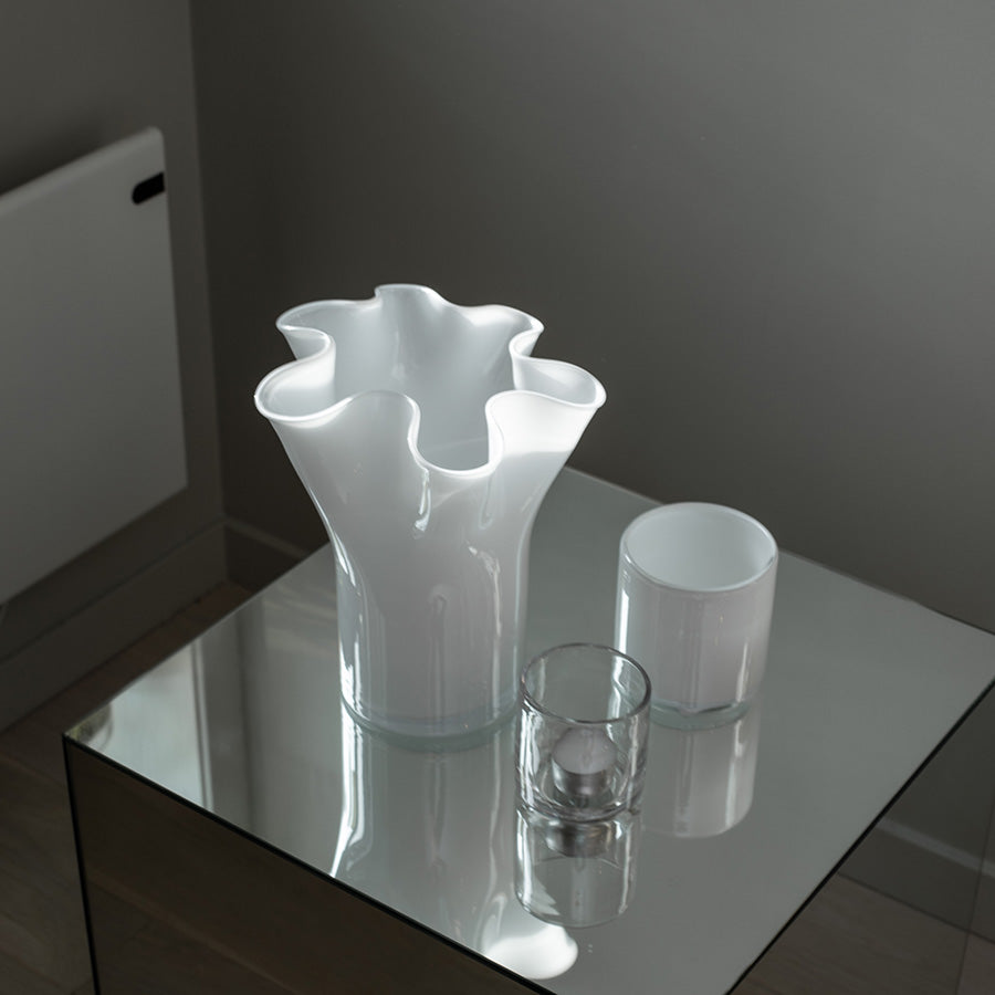 Moderne lyslykt i hvitt glass satt sammen med en dekorativ vase på et speilet bord.