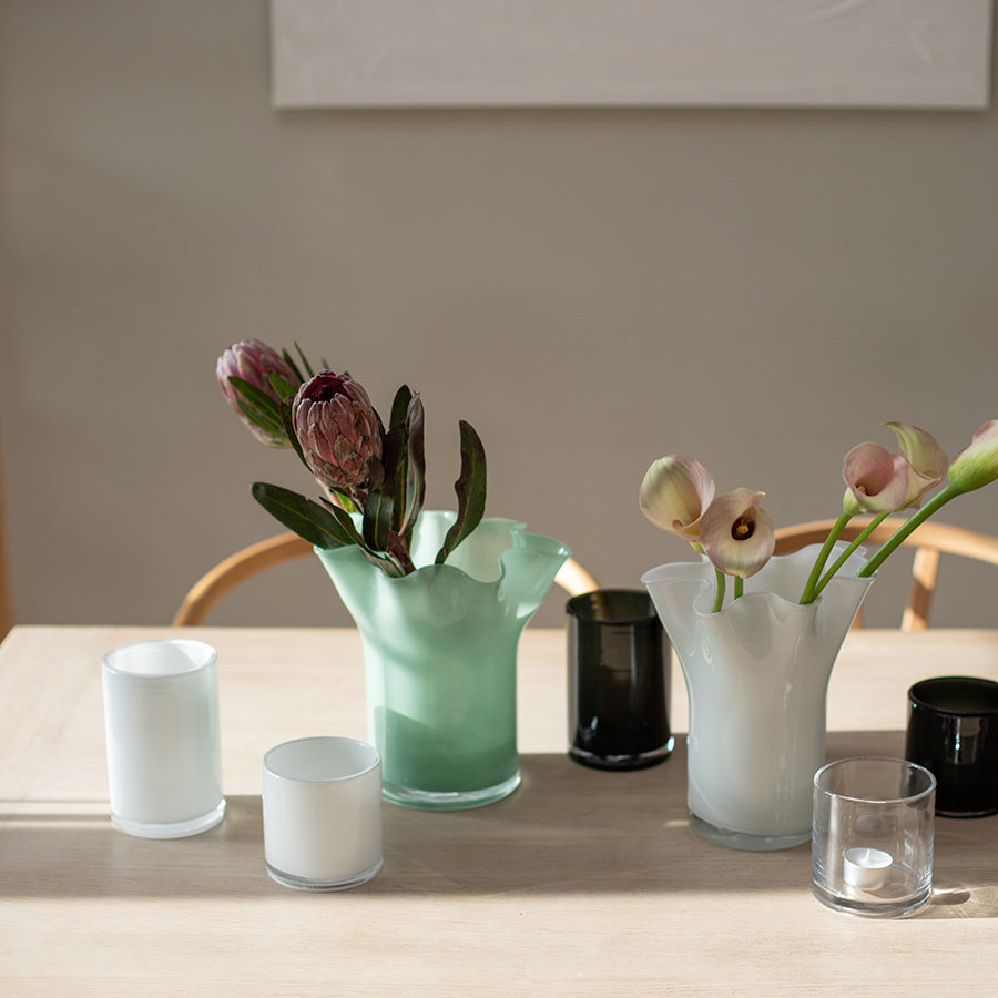 Lyslykter i hvitt og svart glass plassert på et spisebord med blomster, som fremhever elegansen og stilrenheten av lyslykter i interiørdekorasjonen.