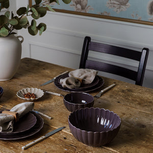 Stilfullt dekket bord med NOVA Lilly Dyp Tallerken 20cm Plomme, elegante plommefargede tallerkener og skåler i rustikk innstilling, perfekt for servering av supper og salater. Dyp tallerken i plommefarge kombinerer karakter med praktisk bruk.