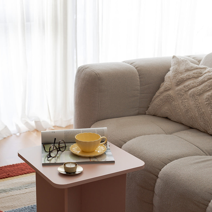 Nova Lilly Kopp og Skål 250ml Gul plassert på et rosa bord ved siden av en beige sofa, skapende en innbydende atmosfære for kaffepause med Kopp og skål.