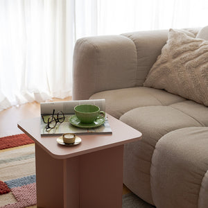 Lilly kopp og skål fra NOVA i grønn farge plassert på et rosa sidebord med en bok og briller, perfekt for en koselig kaffestund. Kopp og skål designet gir en naturlig følelse til borddekkingen.
