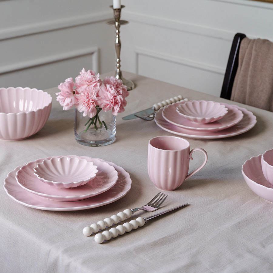 Stilrent dekket bord med Nova Lilly skål i dus rosa, sammen med tallerkener og blomster, perfekt for borddekorasjon.