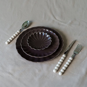 Borddekk med Nova Lilly skål i plommefarge, sammen med lyse tallerkener og bestikk, elegant og moderne bordsetting.