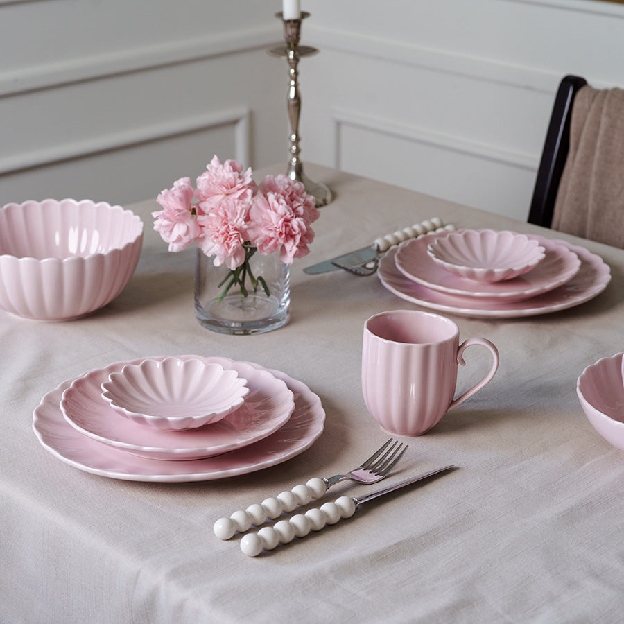 Dekorativt bord med Nova Lilly tallerken i dus rosa sammen med matchende servise og blomster, ideal for spesielle anledninger.