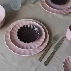 Stabel av Nova Lilly tallerken i dus rosa sammen med en mørk tallerken, fremhever kontrasten i et stilfullt borddekor.