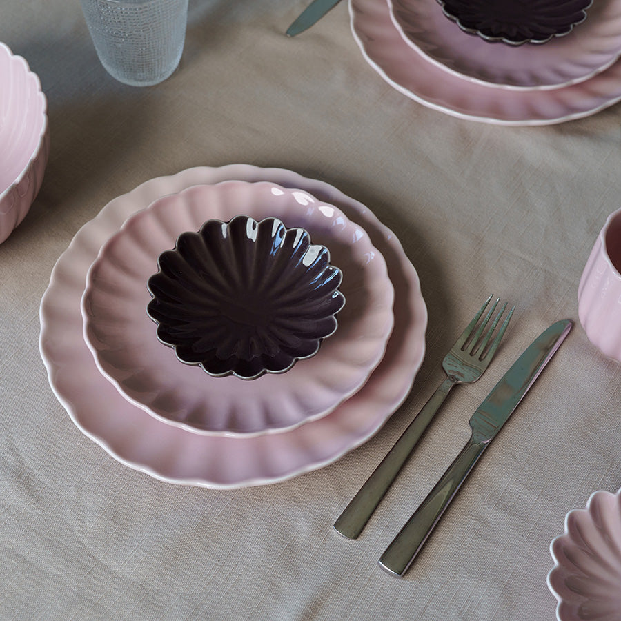 Stabel av Nova Lilly tallerken i dus rosa sammen med en mørk tallerken, fremhever kontrasten i et stilfullt borddekor.