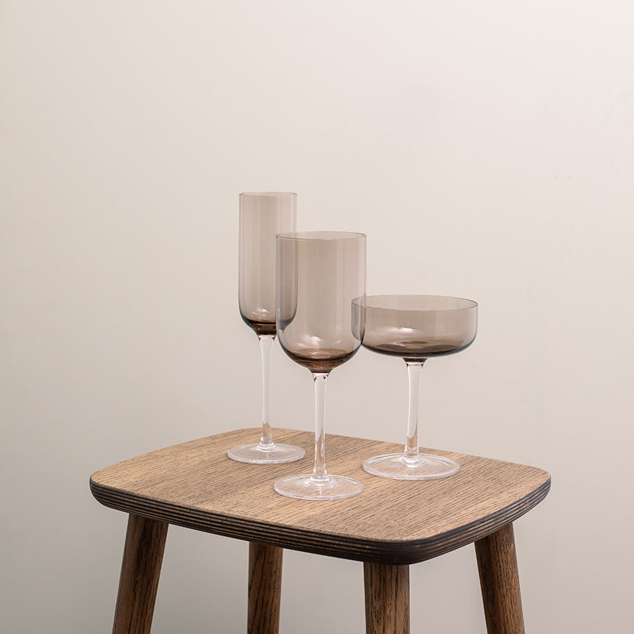 Elegante champagneskåler, champgneglass og vinglass i sotet brunfarge stående på et trebord, ideelle for servering av musserende vin.
