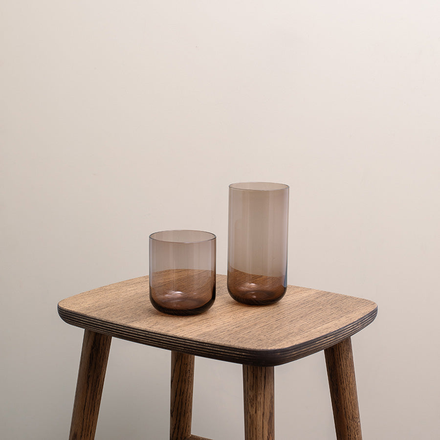 To stilige brune vannglass på et treskjermet bord, perfekte for enhver anledning. Det settet med vannglass fra Nova har en moderne sylinderform og minimalistisk design, og passer til vann, juice eller cocktails.