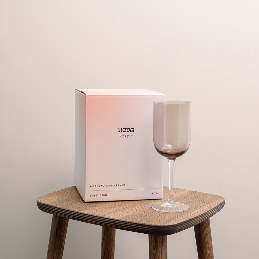 Sotet brunt allround glass fra Nova stående ved siden av esken, plassert på en trehånd, fint designet for borddekking.