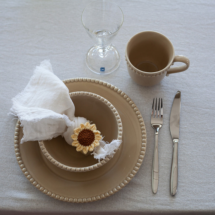 Beige krus i Poppy-kolleksjonen fra Nova, plassert på dekket bord med servietter og bestikk.