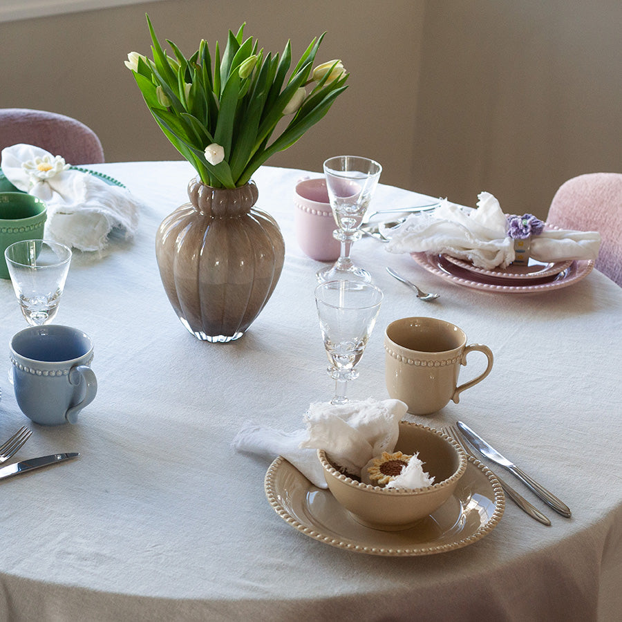 Dekket bord med beige Nova Poppy krus, servise og blomster, skaper en varm og innbydende atmosfære.
