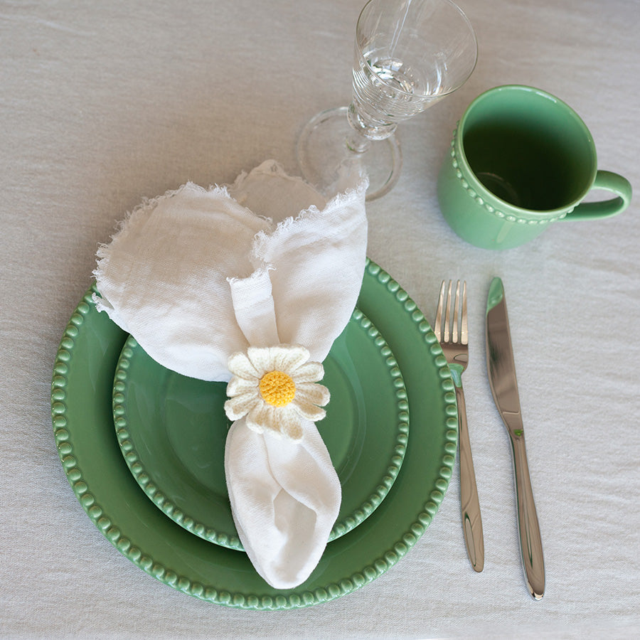 Nærbilde av et grønt Nova Poppy krus på en dekket tallerken, dekorert med en blomst til servietten.