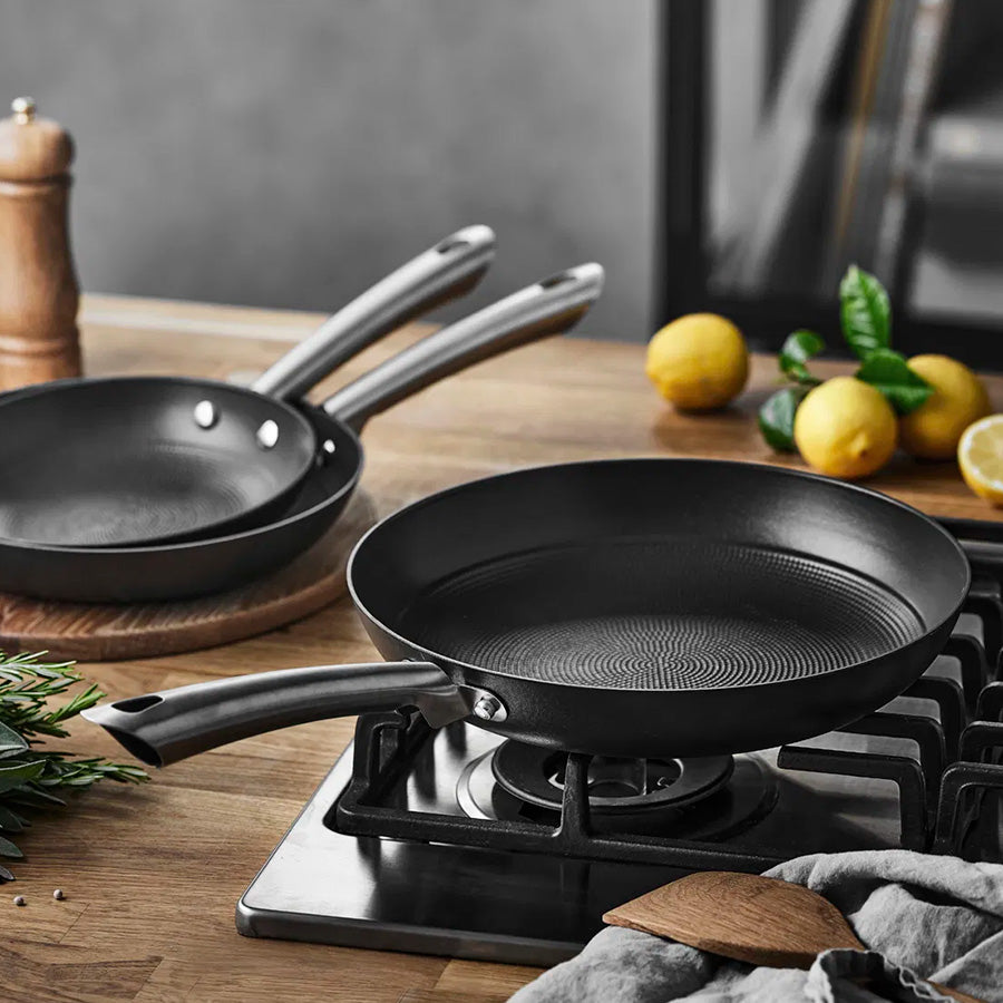 To Pillivuyt Garonne støpejernspanner på komfyren, en med kjøtt og den andre tom, klar til bruk.