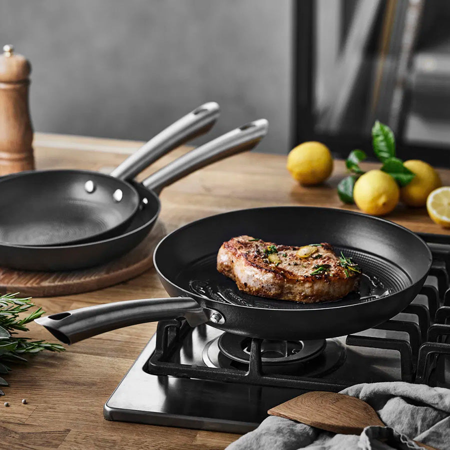 Støpejernspanne som steker en saftig biff på komfyren, viser det ergonomiske rustfrie stålhåndtaket.
