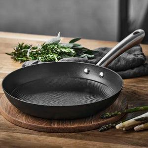 Støpejernspanne med bikubestruktur, presentert på en treplate med grønnsaker i bakgrunnen, ideell for kvalitet matlaging.